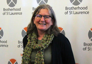 Woman standing in front of a Brotherhood of St Laurence banner