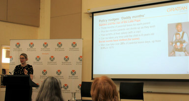 A woman speaking in front of a projected presentation