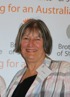 Photograph of Jan Carter. She is standing in front of a sign that says Working for an Australia free of poverty with the BSL logo.