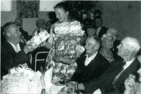 A woman gives wrapped presents to older men at a Christmas party at the Coolibah Club in the 1950s