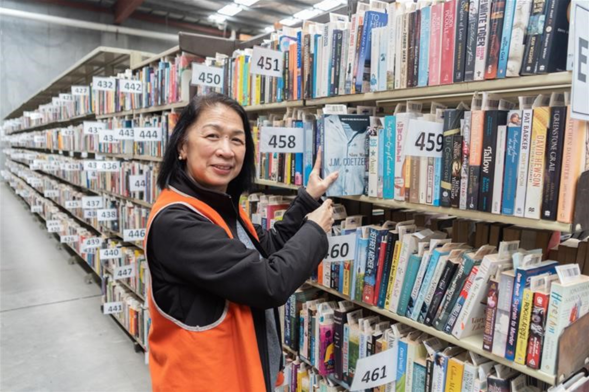 Marilou Belleza holding a book at the new Brotherhood Books warehouse. Behind her are rows of loaded bookshelves