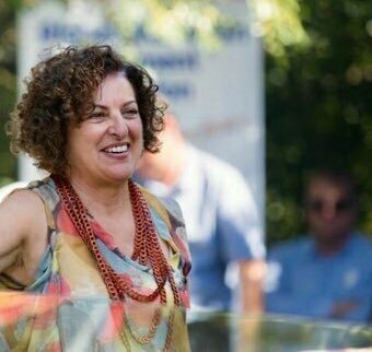 Sarina Greco standing outside and smiling. There is a crowd of people standing nearby.