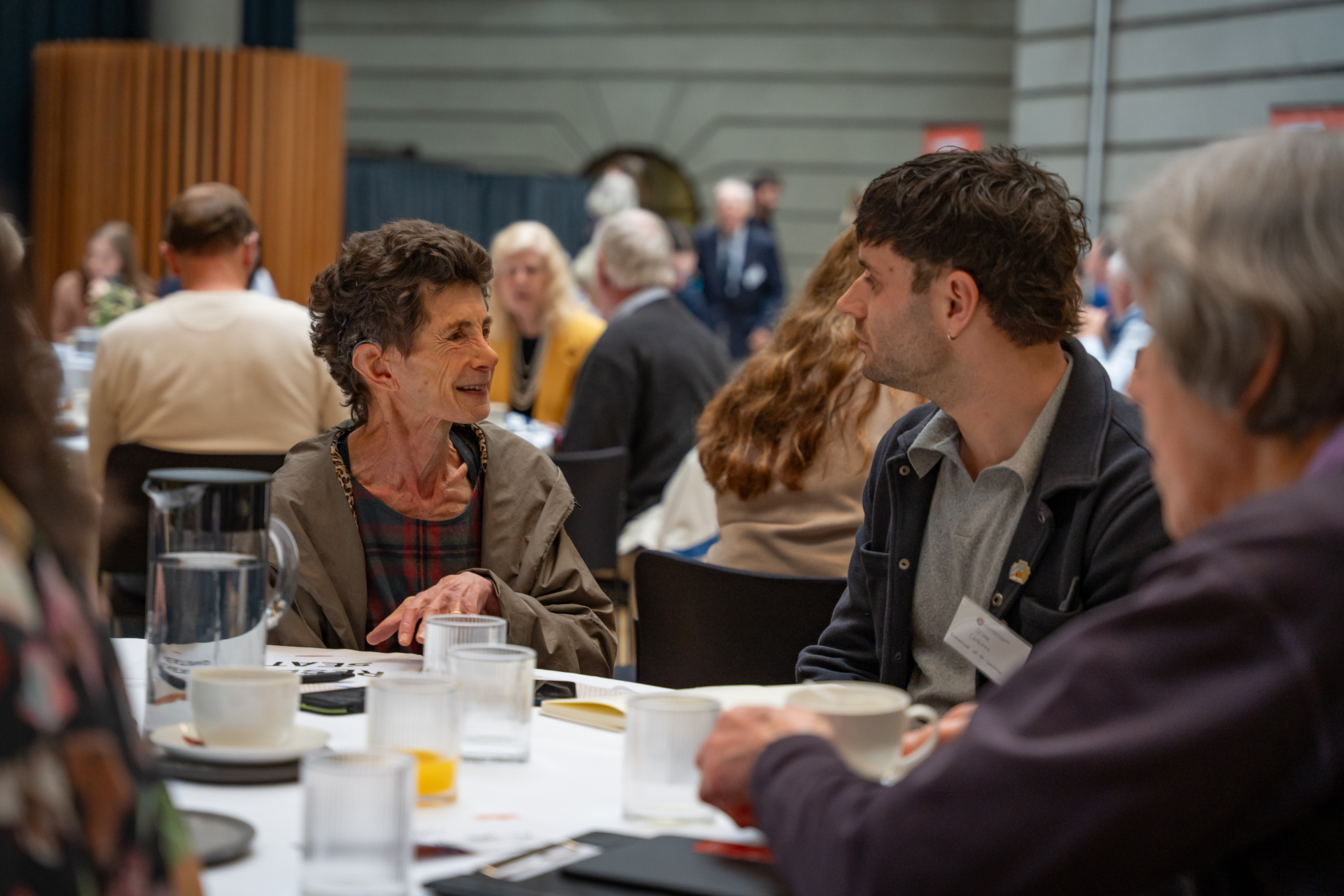 Two people in conversation sitting down in a large room at an event.