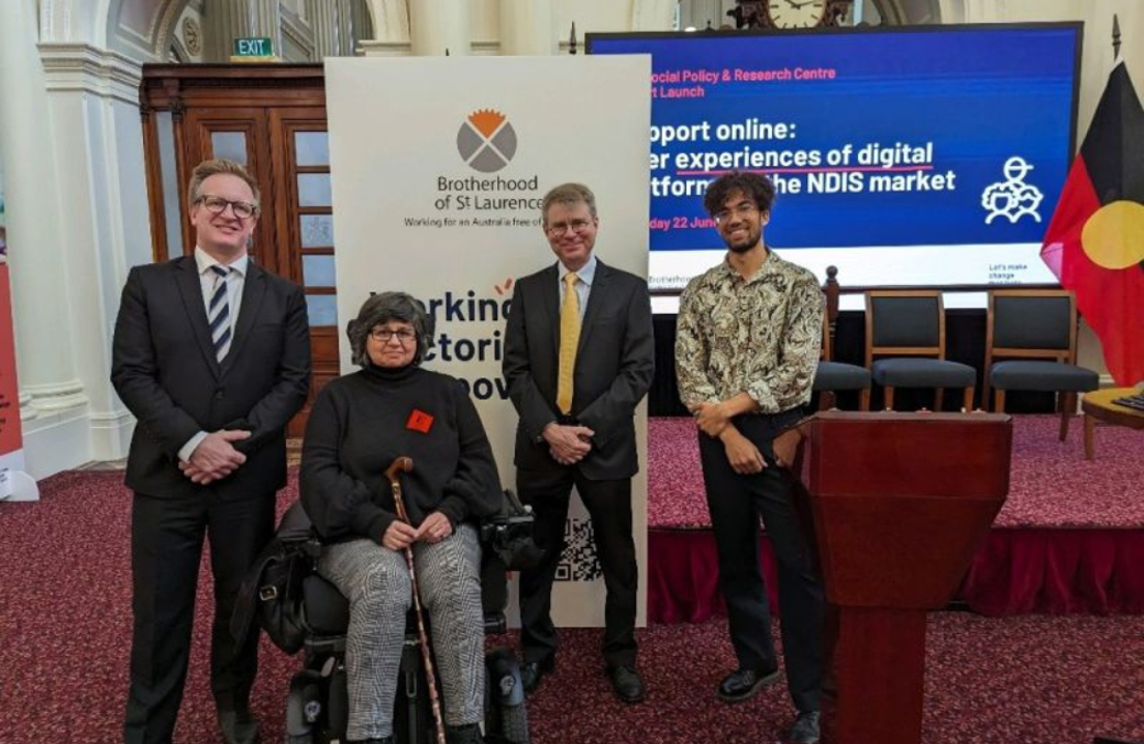 Left to right: Parliamentary Secretary Paul Edbrooke, MP, Georgia Katsikis, Ismo Rama, and Andrew Thies launching our 'Support online: User experiences of digital platforms in the NDIS market' report. They are looking at the camera and smiling. Behind them is a BSL banner and a large digital screen
