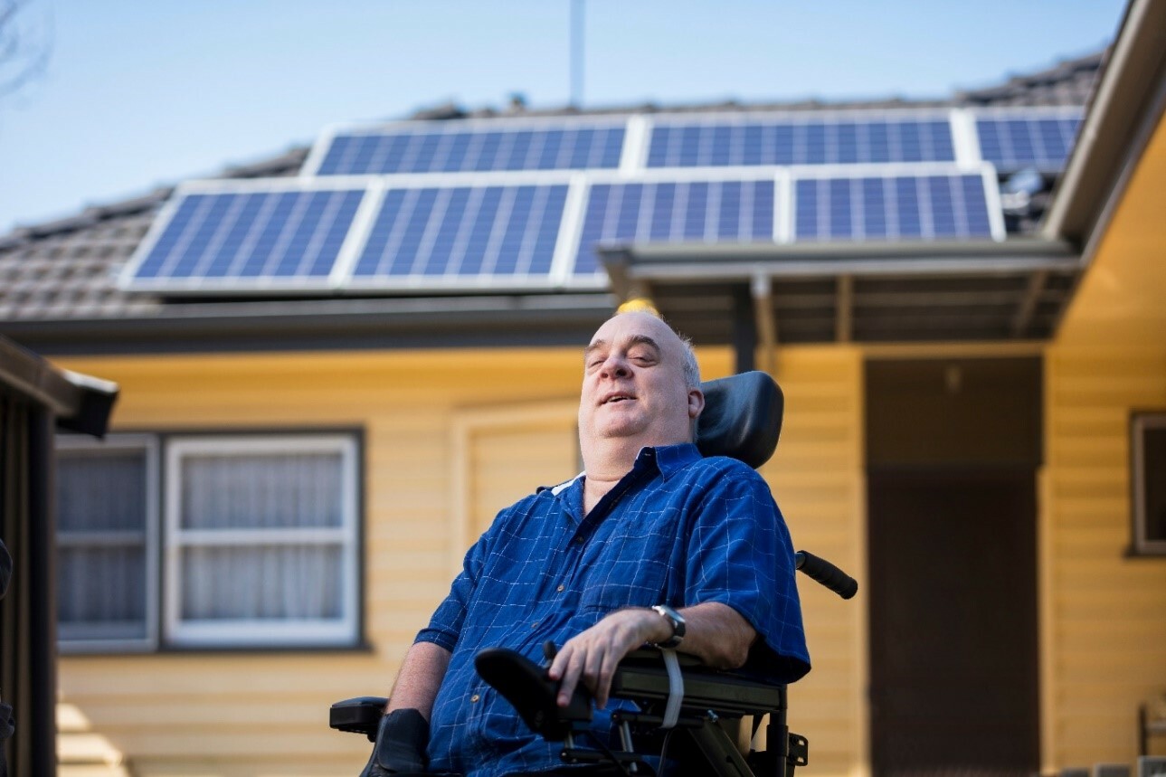 A man in a wheelchair outside a house with solar panels on the roof