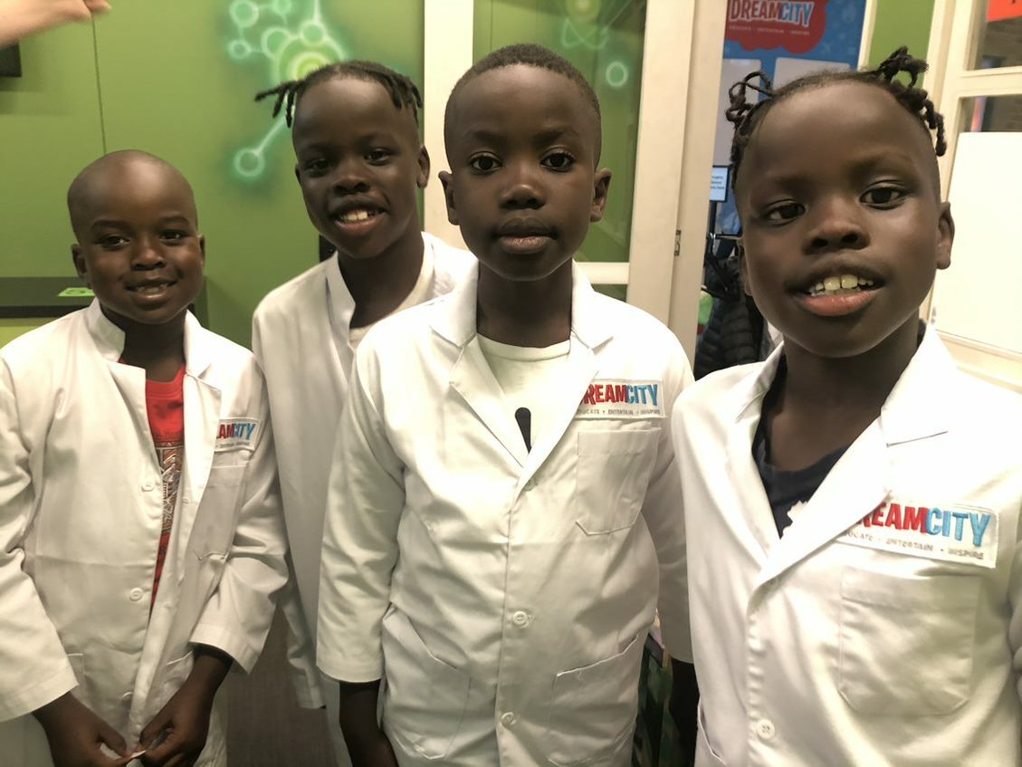 4 young boys stand in white lab coats in class