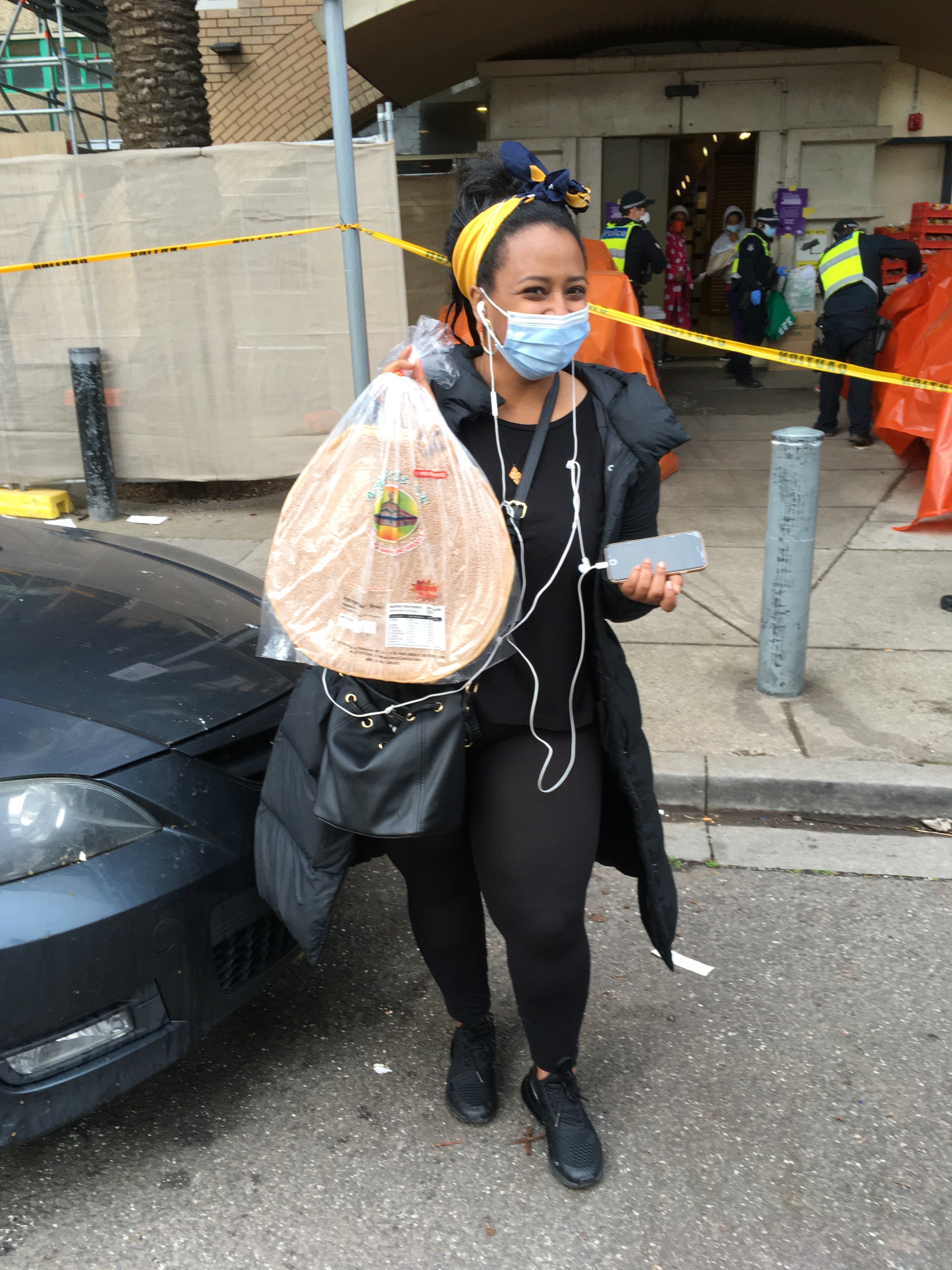 A woman wearing a face mask and carrying bags of food