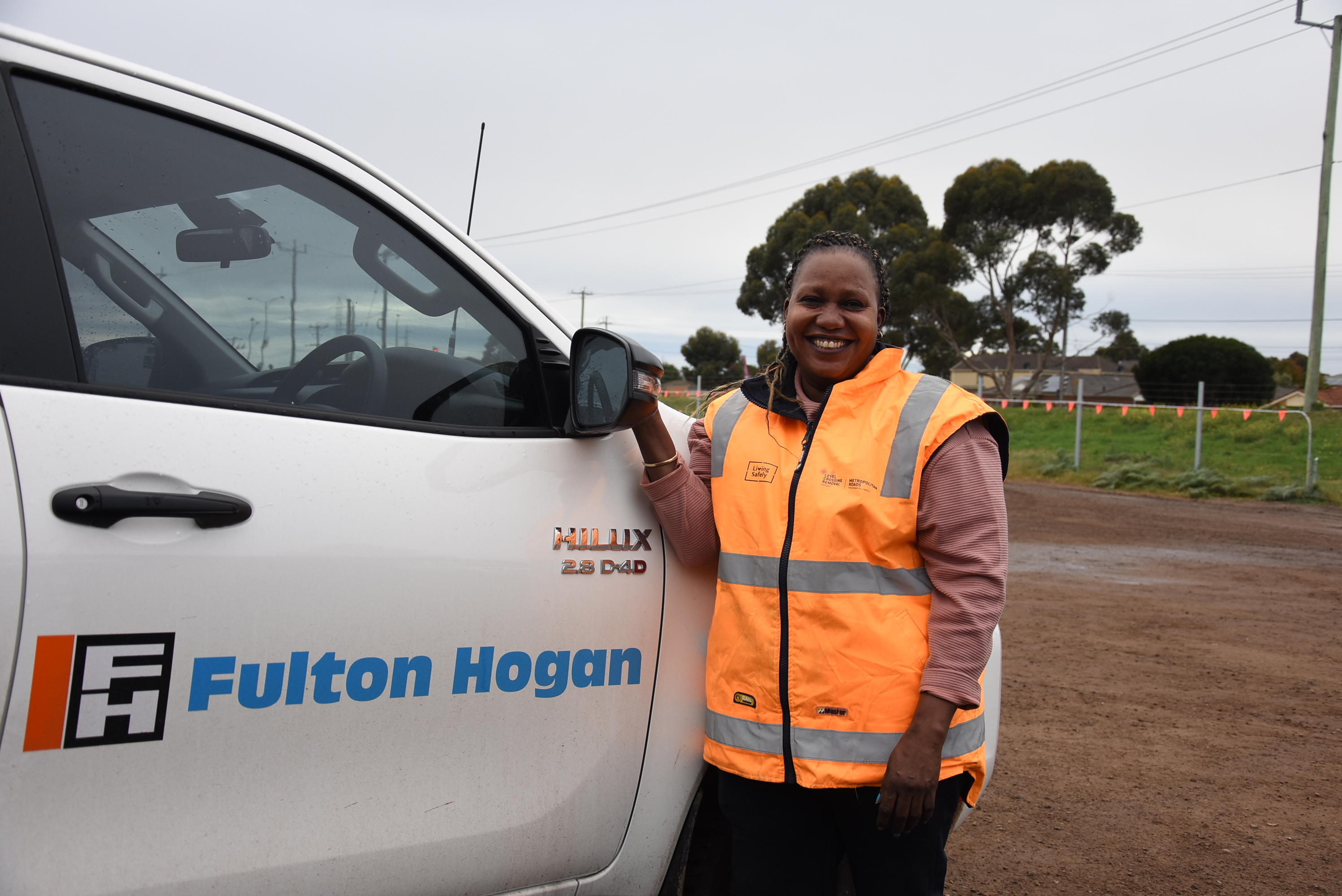 A woman stands in a fluoro vest beside a ute