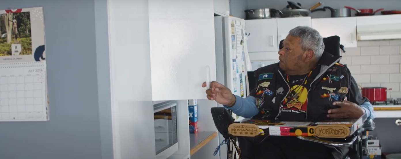 A man in a wheelchair gets items out of a cupboard in a kitchen