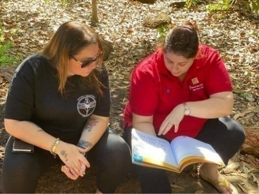 Two women sit outside looking at a course book