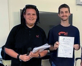 Two man stand together in a classroom, one with a certificate