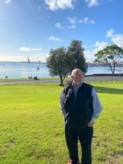 A man standing outside in a park near some water