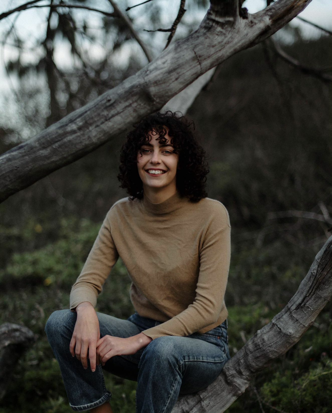 a photo of a woman sitting on a bark of a dead tree