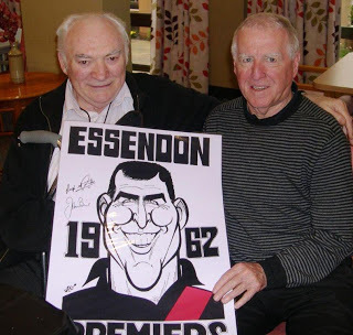 Two older men hold up signed Essendon 1962 poster