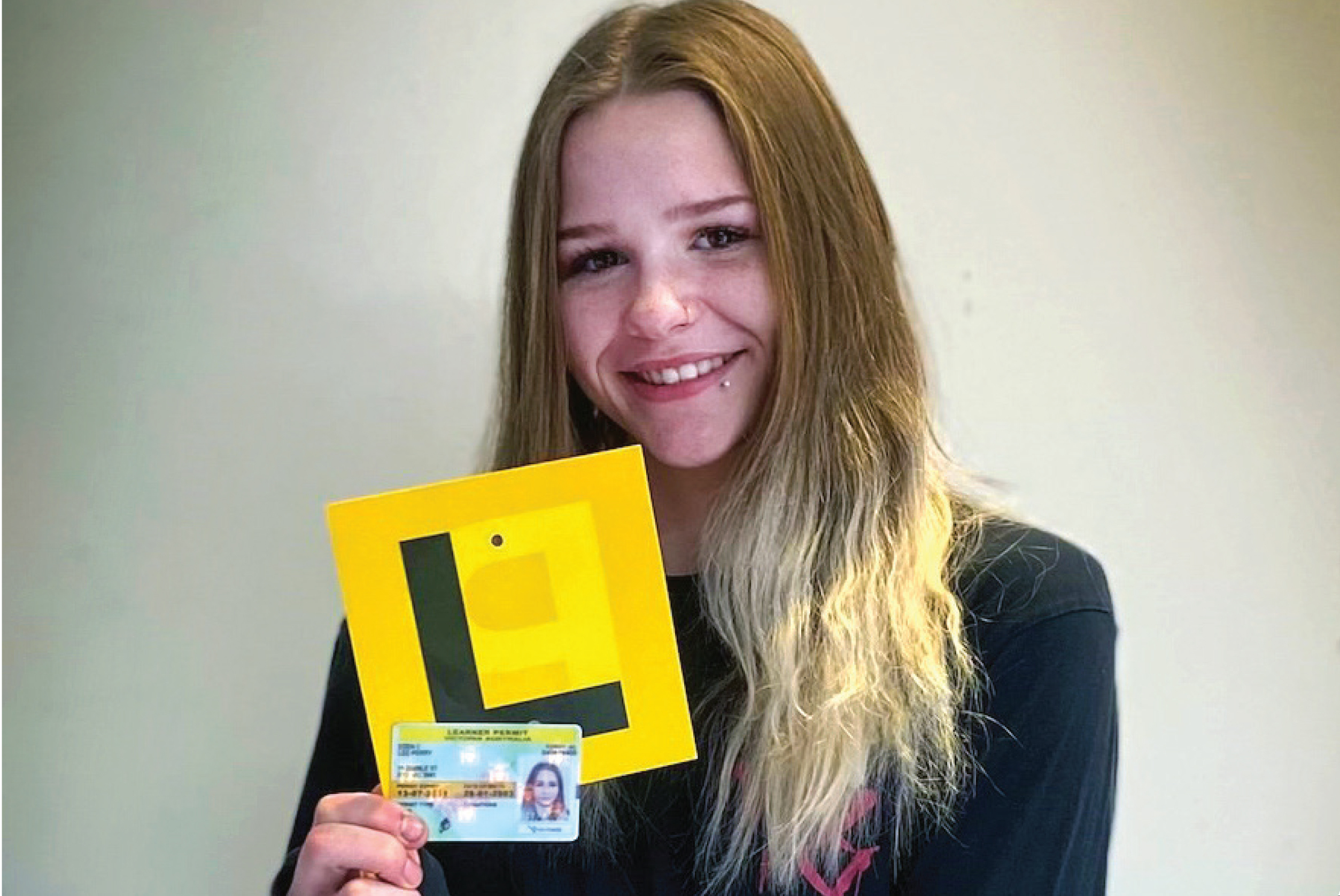 A photo of young woman holding a driver's licence and L plate