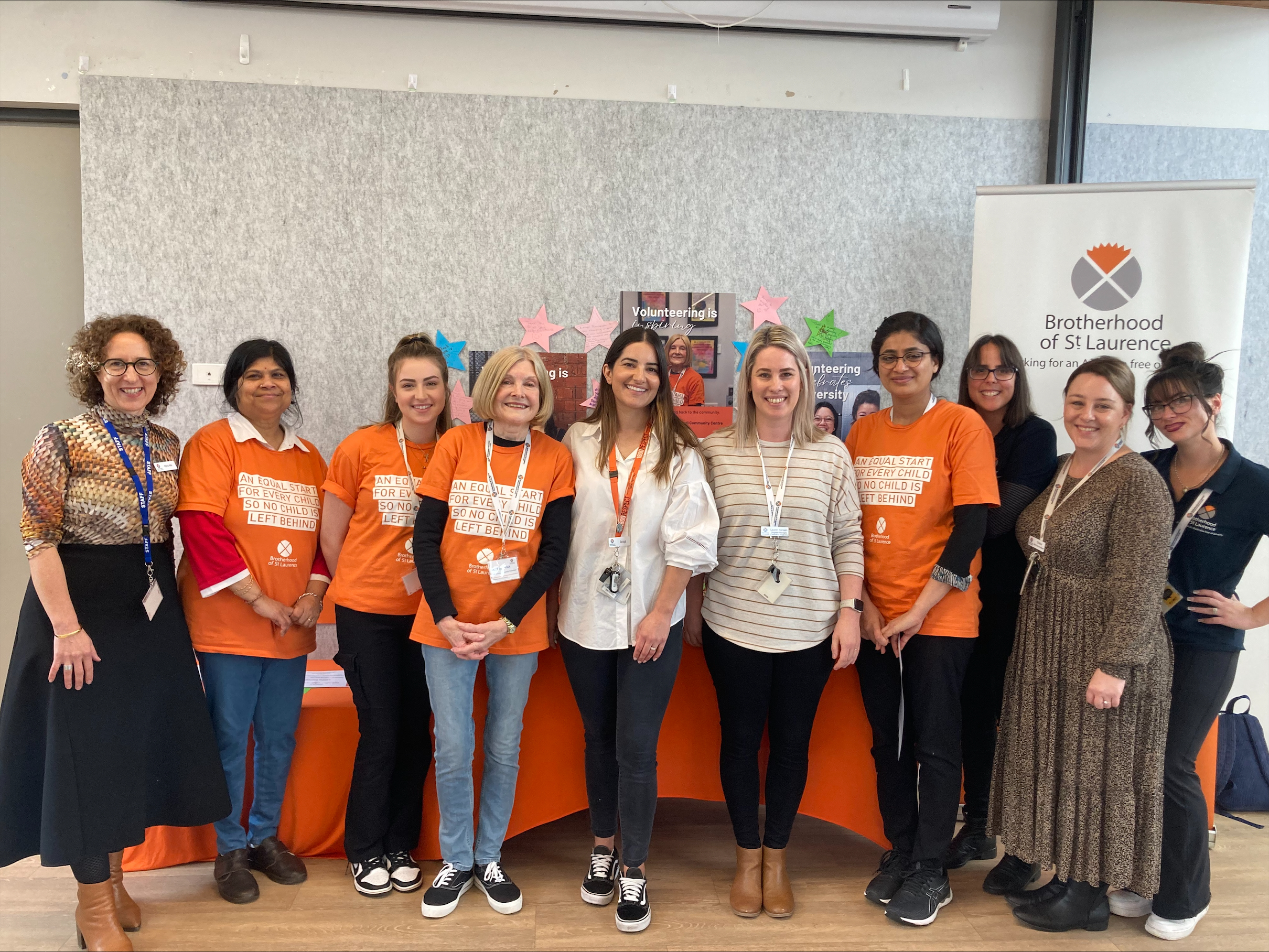 A line of ten women smiling at the camera. Four of the women, volunteers with Jindi, who support our playgroups, are wearing bright orange t-shirts.
