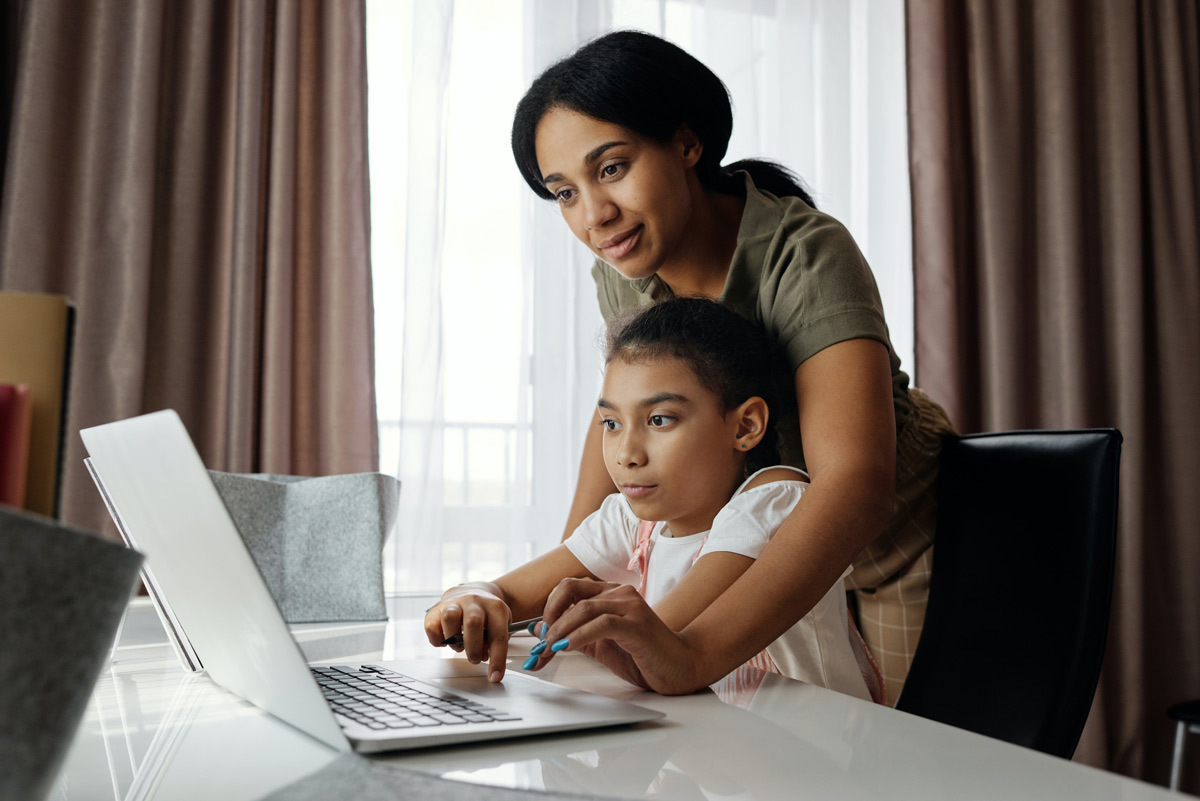 A young girl works on a laptop while her mother helps