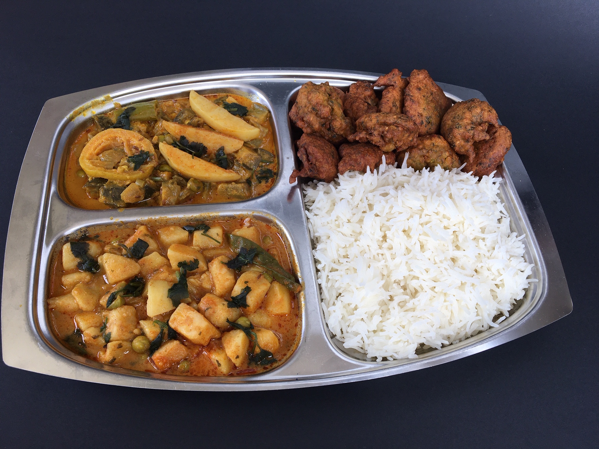 Dish in four sections with rice, pakora and two curries